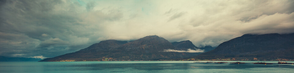 Fjord with blue water in stormy weather. Rocky beach, Norway