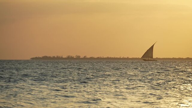 Zanzibar, Tanzania: Slow motion footage of dhow, traditional boat in Zanzibar Archipelago, Tanzania with island in the background at dramatic sunset 