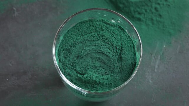 Putting a scoop of green spirulina algae powder into a glass of water, top view
