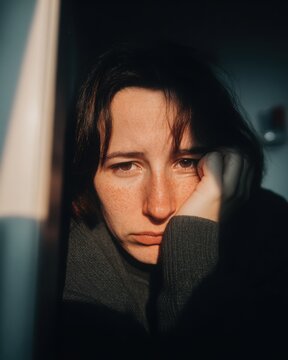 Pensive Woman Leans Head on Hand in Shadowy Light, Contemplative Mood