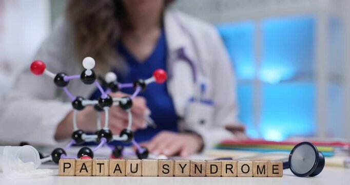 Wooden cubes spell phrase Patau Syndrome near molecule model on table. Genetic doctor writes report explaining severe trisomy condition risks