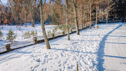 Snow-covered pathway lined with trees and a stone fence in a winter landscape, footprints visible in the fresh snow