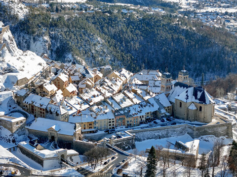 Aerial view of a historic town with snow-covered rooftops nestled against a backdrop of majestic, snow-dusted mountains, Briancon, Provence-Alpes-Cote d'Azur, France.