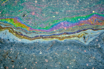 Oil slick creating a rainbow pattern on a wet asphalt surface, indicating pollution