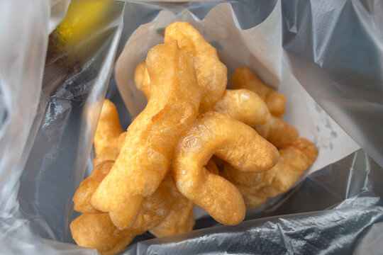 Traditional Thai breakfast of golden brown Patongko or Chinese deep-frie dough in a plastic bag, street food snack with crispy texture and soft inside, macro shot with selective focus depth.