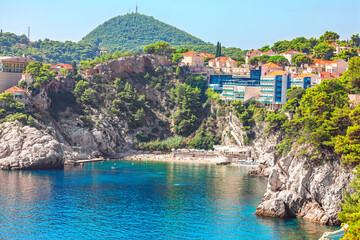 Bellevue Beach in Dubrovnik, stunning secluded pebble cove with turquoise water. Surrounded by steep cliffs and lush hillside topped with terracotta roofed buildings, popular swimming spot in Adriatic