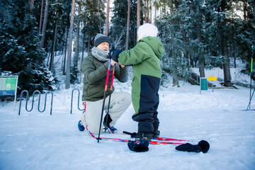 Father helping son with skis in Finnish forest. Active family winter vacation, Scandinavia. Nordic lifestyle, parenting, outdoor sports. Real people.