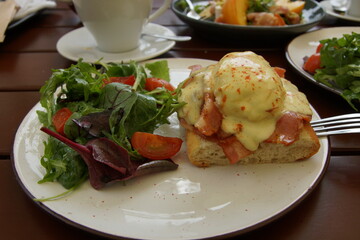 Eggs Benedict on Toasted Bread with Crispy Bacon, Hollandaise Sauce and Fresh Side Salad with Cherry Tomatoes