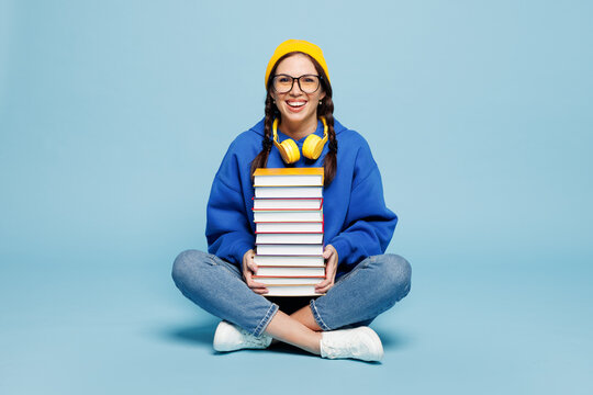 Full body happy young smart reader woman student wear casual clothes yellow backpack bag sit with stack of books isolated on pastel plain light blue color background. High college lifestyle concept.