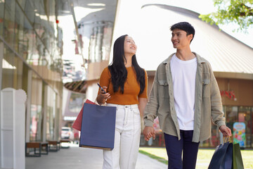 Obraz premium Beautiful couple enjoy shopping together, young couple holding shopping bags, Shopping, Couple, Love, Man and woman with shopping bags are hugging and smiling while walking down the street