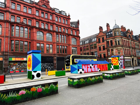 Colorful urban Fred Aldous and Andrew Wolfenden art on a Manchester Stevenson Square street with painted benches and a bright yellow bus