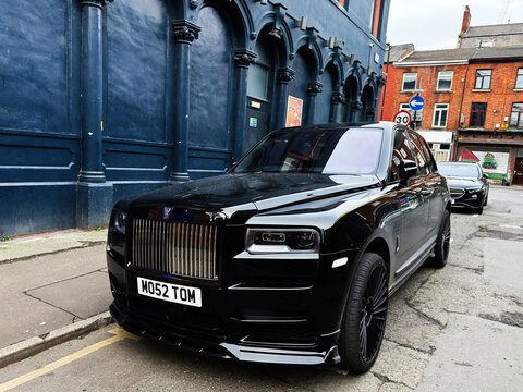 Luxurious black Rolls-Royce Cullinan SUV parked on a Manchester street near blue historic building