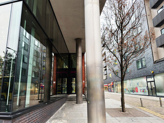 Naklejka premium Modern glass building entrance on Manchester street with trees and urban storefront