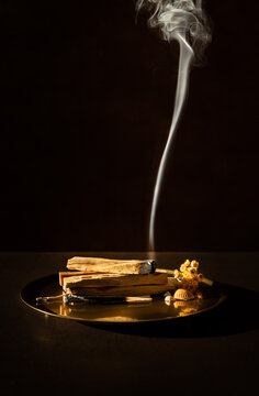Bois de Palo Santo br&ucirc;lant sur un plateau en bronze, fum&eacute;e blanche verticale, belle lumi&egrave;re, fond fonc&eacute;