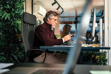 Professional man concentrating on task while using computer with ergonomic mouse in modern eco-friendly workspace