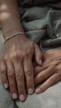 Vertical video: Placing top hand pearlbracelet settling over lower hand on throw at home comforting