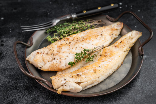 Roasted flaky whitefish fillets with fresh thyme, overhead food photo on moody dark background with copy space.