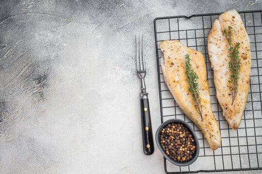 Roasted flaky whitefish fillets with fresh thyme, food photography on cooling rack over light stone background.