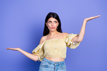 Young woman in yellow off shoulder blouse poses with arms out against purple background for fashion...