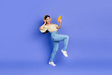 Young woman dancing smiling with headphones and phone against purple background for bold lifestyle...