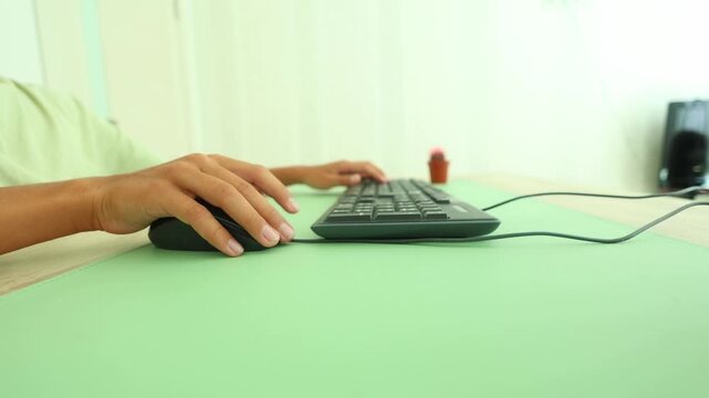 Side angle view of hands typing and using a mouse on a mint green desk mat, subtle cactus in background, highlighting focused digital work, ergonomic setup