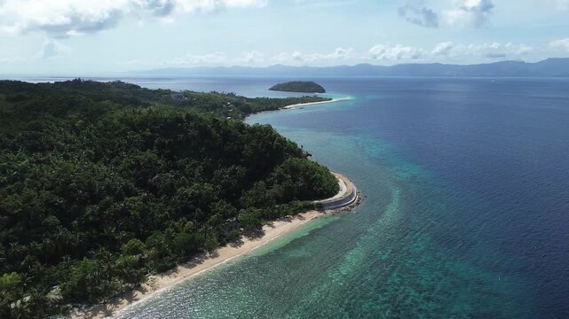 Drone aerial of a tropical coastal road with hills on Romblon, Philippines, featuring Bangug Island in the background, lush greenery, and scenic seaside landscapes.