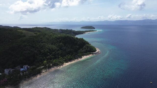 Cinematic aerial view of the coast of Romblon Philippines with Bangug Island in the background showing crystal clear turquoise water tropical shoreline and calm sea under a clear blue sky on sunny day