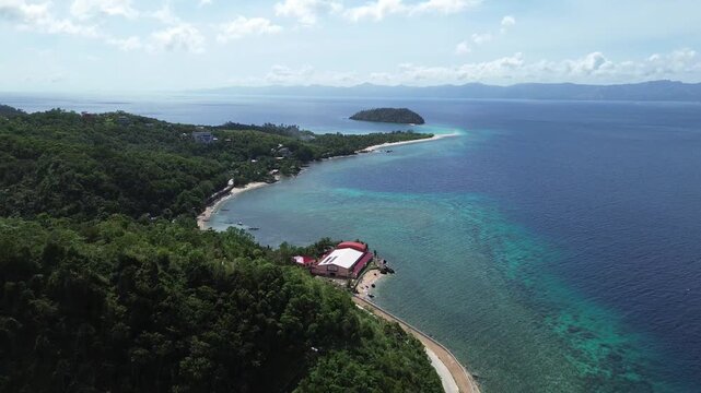Cinematic aerial view of the coast of Romblon Philippines with Bangug Island in the background showing crystal clear turquoise water tropical shoreline and calm sea under a clear blue sky on sunny day