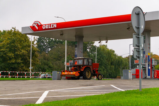 Orlen gas station in Poland with fuel price signage, Stop Cafe shop and red farm tractor at the pump, modern petrol station infrastructure under cloudy sky.