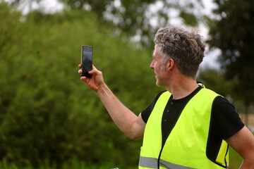 Mann fotografiert in Leuchtweste mit dem Handy