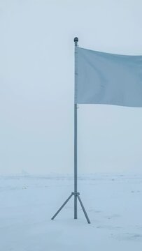 Vertical video: Waving pale blue flag on metal pole with tripod on snow plain, wind lifting ripples