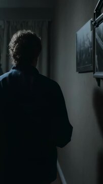 Vertical video: Pausing at door turning, man walking down narrow hall toward curtain in dark jacket