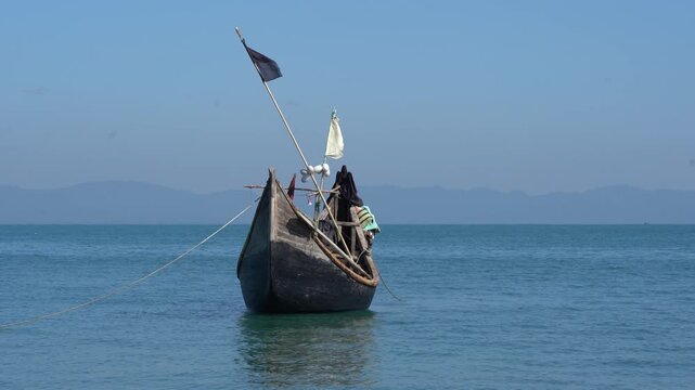 Anchored wooden fishing boat with rope on calm blue sea, Bay of Bengal, Bangladesh