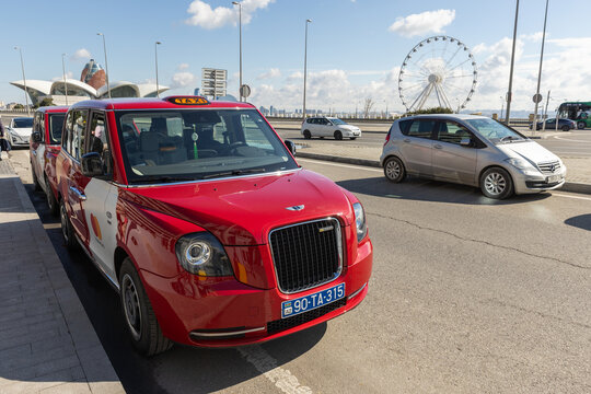 A red taxi sits parked along a sunny coastal promenade