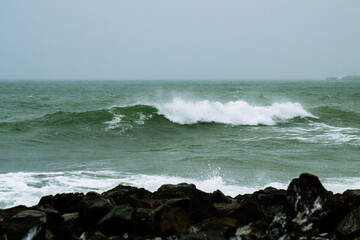 Fototapeta premium turbulent green ocean waves crashing onto a rocky shore, sending white foam and spray into the air.