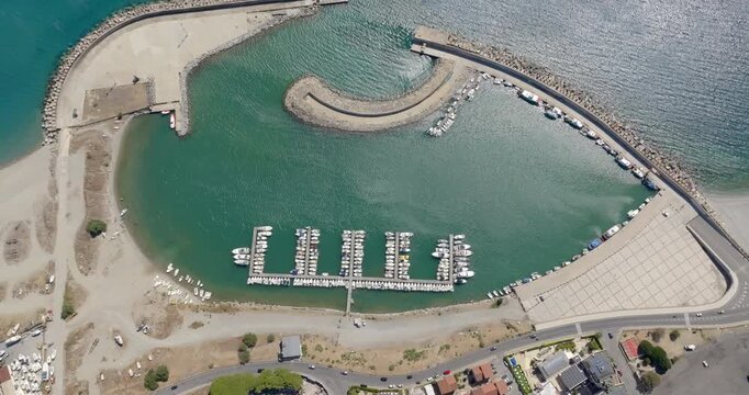 Aerial zenithal view of the Catanzaro Lido port, located on the Ionian coast of Calabria, Italy. Many small boats anchored in the clean, blue marina. It is a sunny summer morning.