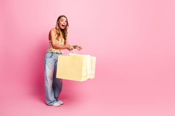 Obraz premium Young woman with shopping bags in pink studio smiling and promoting fashion and lifestyle shopping