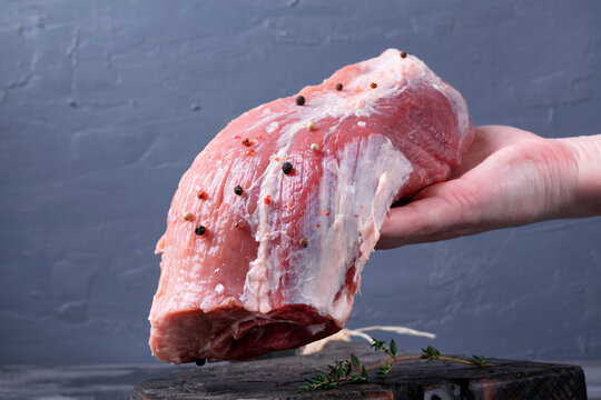Raw pork neck meat with salt and peppercorns is held in a woman's hand on a gray background. Preparing meat for cooking. Fresh farm products