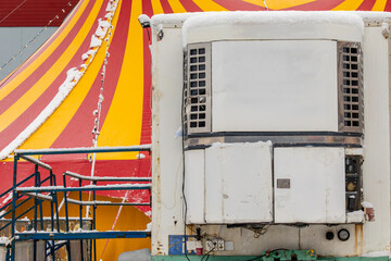 Striped big-top tent stands in the cold season while a utility trailer with equipment shows the operational side of an entertainment venue. The image conveys seasonal performance business, temporary i