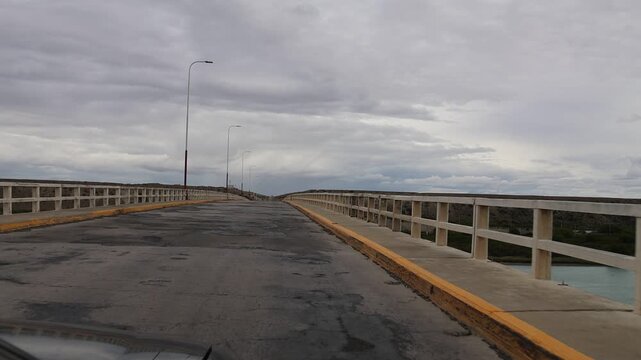 Slow-motion clip filmed from inside a moving car showing the front of the car as it drives over a bridge with many patches in the asphalt