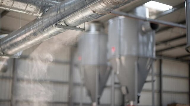Medium shot of overhead galvanized air ducts with blurred background highlighting dust particles swirling near large cyclone separators indoors.
