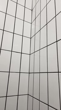Corner of a white glossy ceramic tiled wall with dark grout lines creating a strong geometric perspective.