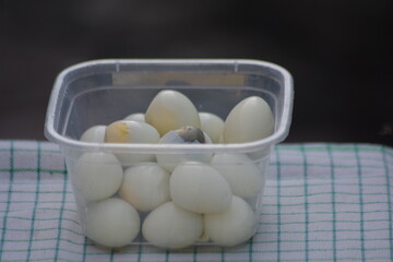 Peeled quail eggs in clear plastic container on kitchen towel