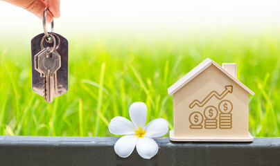 Wooden house model with house key in girl hand over blurred green grass background, property investment business concept