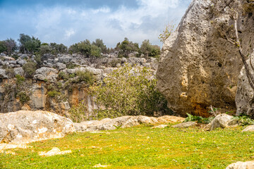Strikingly textured karst landscape features massive, weathered limestone boulders rising dramatically above a carpet of vibrant green spring grass in a hidden pocket of nature. Turkey, Mersin