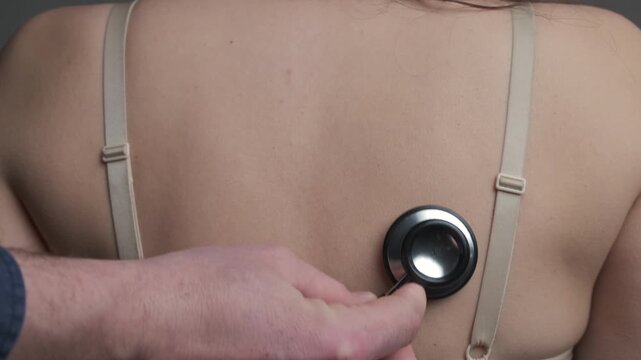 Female Patient Back With Stethoscope During Lung Auscultation, Male Clinician Hand Holding Chest Piece Against Upper Back, Bra