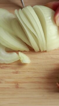 Close-up of woman&rsquo;s hands slicing a raw peeled yellow onion into half-circle slices on a wooden cutting board