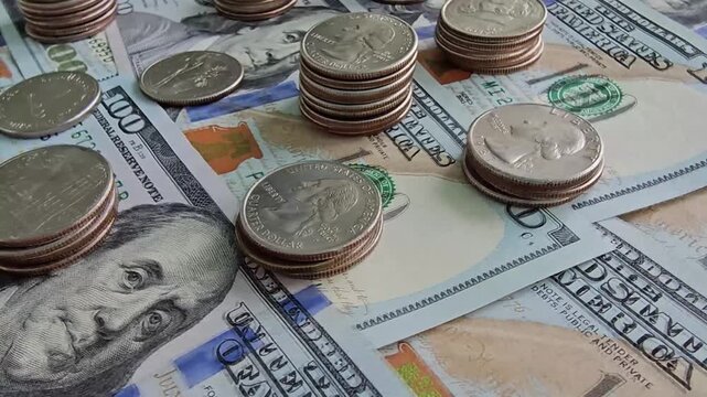 Gathering stacks of coins and bills showing one hundred dollar notes and quarters on a flat surface