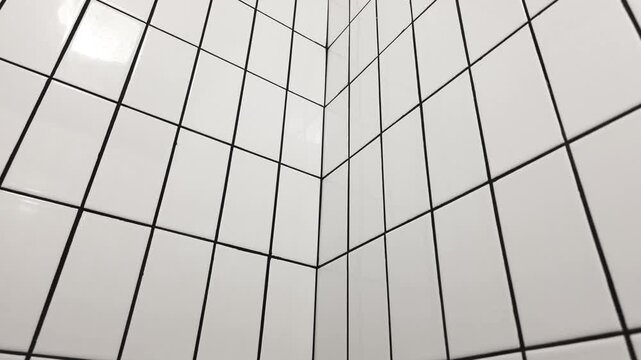 Corner of a white glossy ceramic tiled wall with dark grout lines creating a strong geometric perspective.