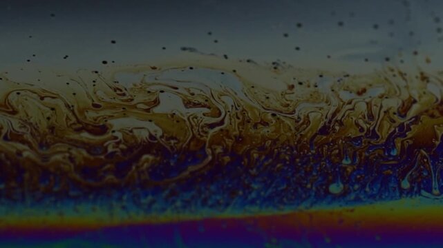 Macro video of a soap bubble surface showing dancing iridescent colors and smooth fluid motion. Abstract liquid patterns shift organically across a dark background, creating  ethereal, calming visual